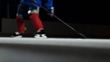 Nahaufnahme-Des-Pucks-Auf-Dem-Eis-Und-In-Zeitlupe-Fährt-Der-Eishockeyspieler-Hoch,-Der-Schnee-Fliegt-In-Die-Kamera-Und-Er-Nimmt-Den-Puckschläger
